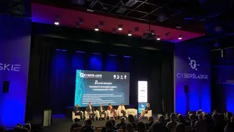 Conference room filled with audience. 5 people talking on stage.