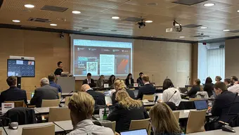 Group of people sitting in a conference room. They're watching a presentation.