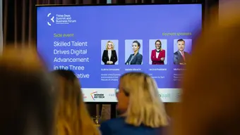 People watching a presentation. On the slide they see colference speakers.